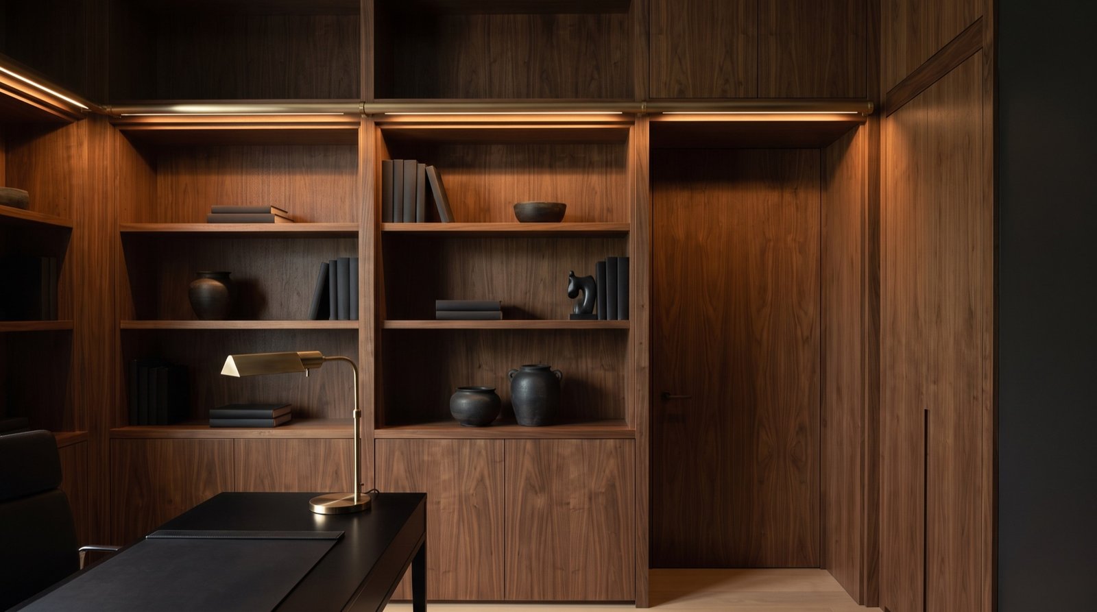 Finished home office library wall in walnut with a concealed door and bronze rail lighting